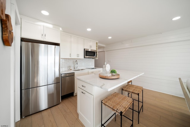 kitchen featuring a breakfast bar area, a sink, white cabinets, appliances with stainless steel finishes, and light wood-type flooring