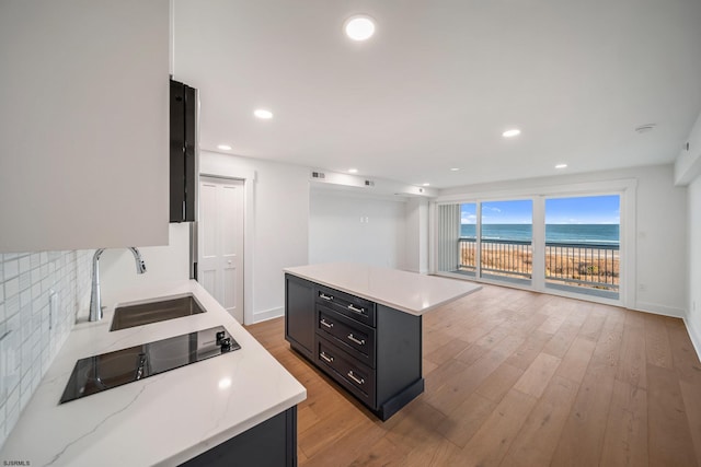 kitchen with tasteful backsplash, light wood-style flooring, dark cabinetry, a sink, and recessed lighting