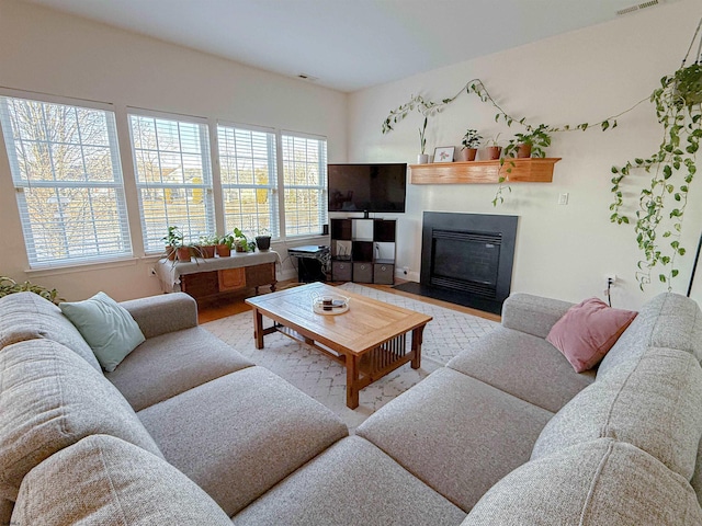 living room with a fireplace with flush hearth, visible vents, a wealth of natural light, and wood finished floors