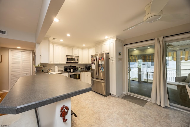 kitchen with a peninsula, a sink, white cabinetry, appliances with stainless steel finishes, and dark countertops