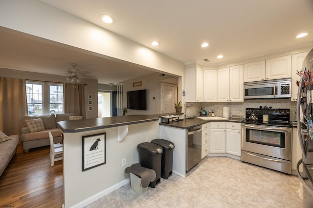 kitchen featuring a peninsula, white cabinetry, open floor plan, appliances with stainless steel finishes, and dark countertops