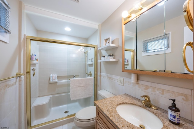 full bathroom featuring a stall shower, wainscoting, toilet, vanity, and tile walls