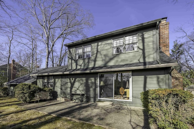 back of house with a patio area, a shingled roof, and a chimney