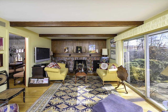 living area featuring beamed ceiling, a brick fireplace, wood finished floors, and visible vents