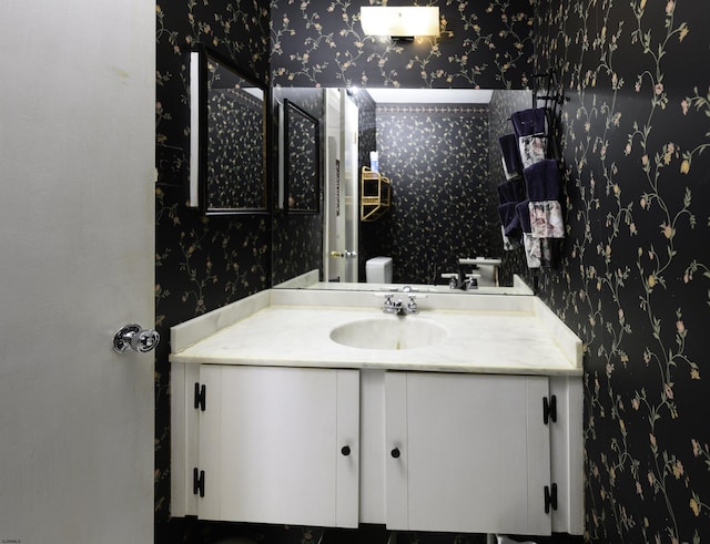 bathroom featuring toilet, vanity, and wallpapered walls