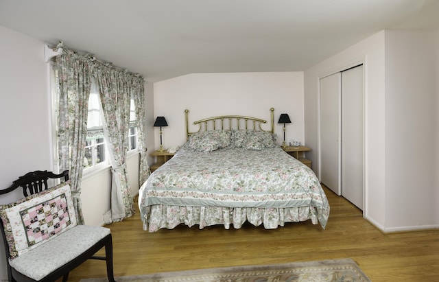 bedroom featuring a closet, vaulted ceiling, baseboards, and wood finished floors