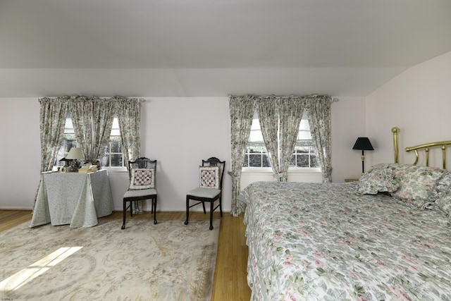 bedroom featuring lofted ceiling, multiple windows, baseboards, and wood finished floors