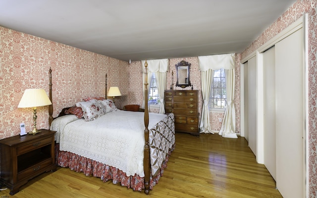 bedroom featuring wood finished floors, two closets, and wallpapered walls