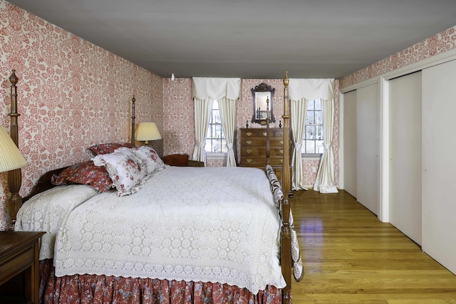 bedroom featuring wood finished floors, multiple windows, two closets, and wallpapered walls