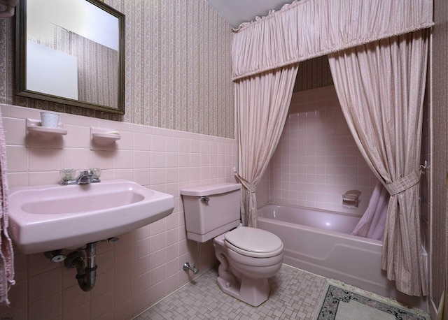 bathroom with tile walls, wallpapered walls, toilet, wainscoting, and tile patterned floors