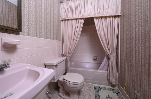 bathroom with wallpapered walls, tile walls, wainscoting, toilet, and a sink