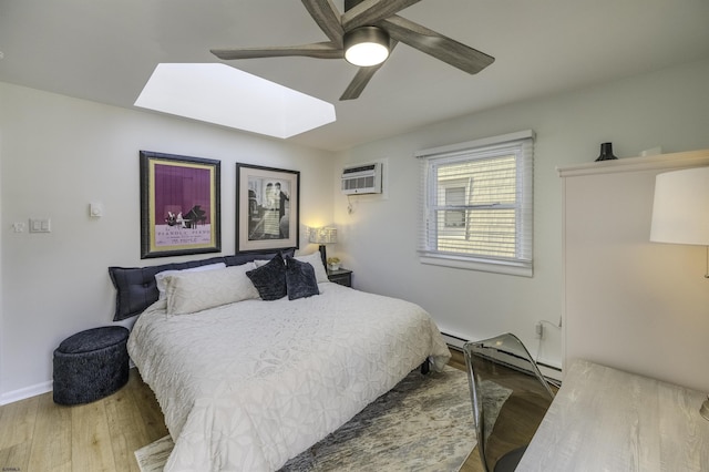 bedroom with a skylight, wood finished floors, a ceiling fan, baseboards, and a wall mounted air conditioner