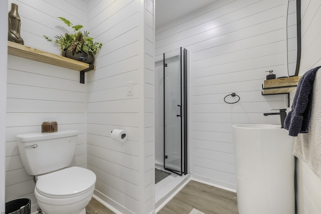 full bath with toilet, a stall shower, wooden walls, wood finished floors, and baseboards