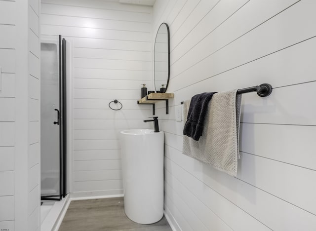 bathroom featuring wooden walls, a shower stall, and wood finished floors