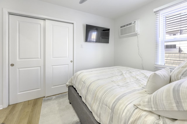 bedroom featuring light wood-type flooring, a closet, and an AC wall unit