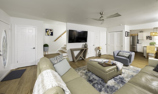 living area featuring a ceiling fan, stairway, baseboards, and wood finished floors