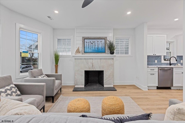 living area featuring recessed lighting, a premium fireplace, visible vents, baseboards, and light wood finished floors