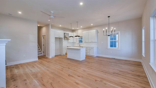 kitchen featuring recessed lighting, ceiling fan with notable chandelier, a kitchen island, wall chimney range hood, and light wood-type flooring