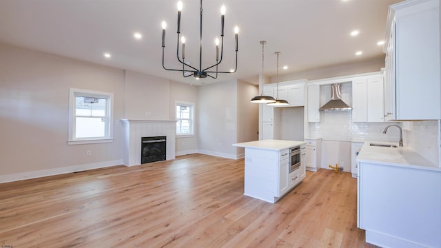 kitchen featuring a fireplace, a sink, white cabinets, wall chimney range hood, and tasteful backsplash