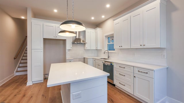 kitchen featuring a center island, light wood-style floors, a sink, wall chimney range hood, and dishwasher