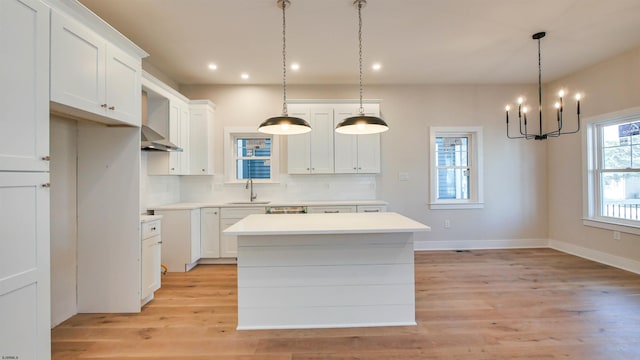 kitchen featuring a center island, decorative backsplash, light wood-style floors, white cabinetry, and a sink