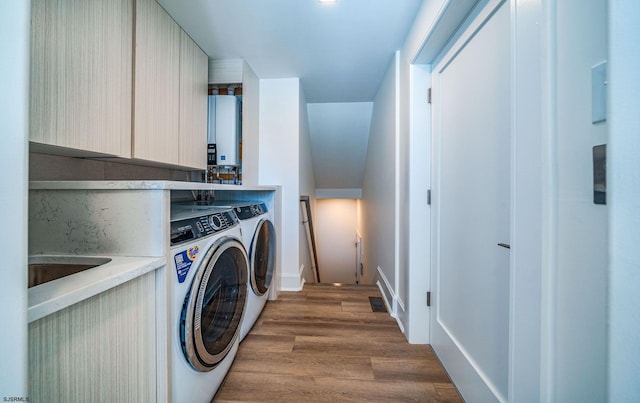 clothes washing area featuring water heater, cabinet space, visible vents, wood finished floors, and washer and dryer