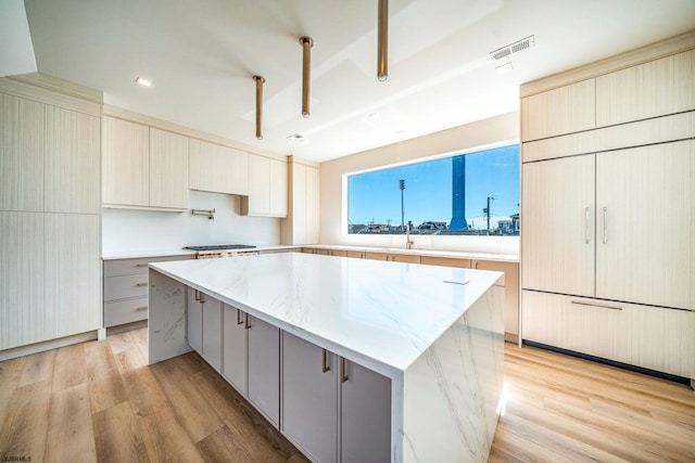 kitchen with light wood finished floors, a spacious island, modern cabinets, and light stone counters