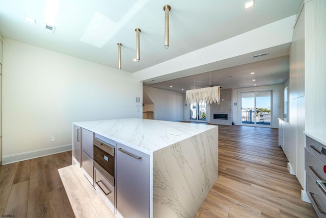 kitchen featuring visible vents, light wood-style floors, open floor plan, a kitchen island, and light stone countertops