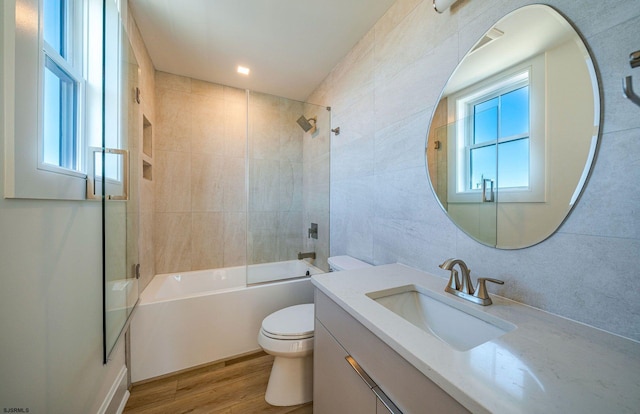 full bathroom featuring toilet, bath / shower combo with glass door, wood finished floors, vanity, and tile walls