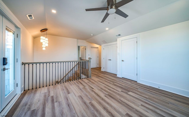 empty room featuring lofted ceiling, visible vents, baseboards, and wood finished floors