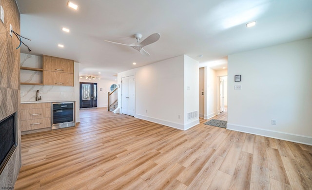 unfurnished living room featuring ceiling fan, wine cooler, a sink, visible vents, and light wood-style floors