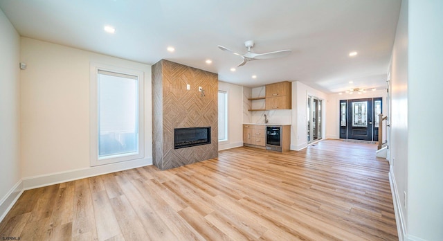 unfurnished living room featuring light wood finished floors, baseboards, wine cooler, a fireplace, and recessed lighting