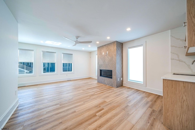 unfurnished living room featuring light wood-style floors, a tile fireplace, a sink, and baseboards