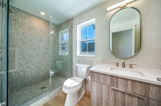 bathroom featuring toilet, tiled shower, tile walls, and wood finished floors