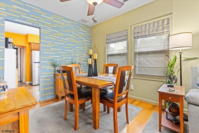 dining area with light wood finished floors, wallpapered walls, baseboards, ceiling fan, and an accent wall