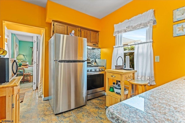 kitchen with brown cabinetry, light countertops, stainless steel appliances, under cabinet range hood, and backsplash