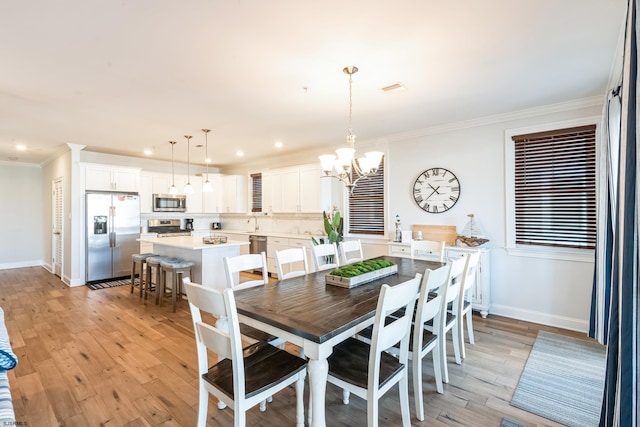 dining space with visible vents, baseboards, light wood-style floors, ornamental molding, and an inviting chandelier