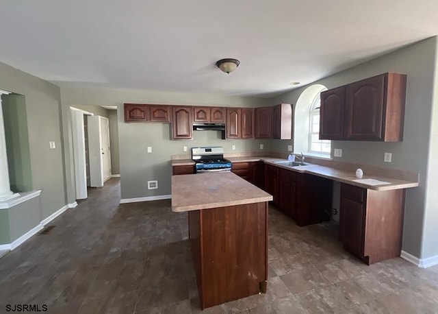 kitchen featuring gas range, a center island, light countertops, under cabinet range hood, and a sink