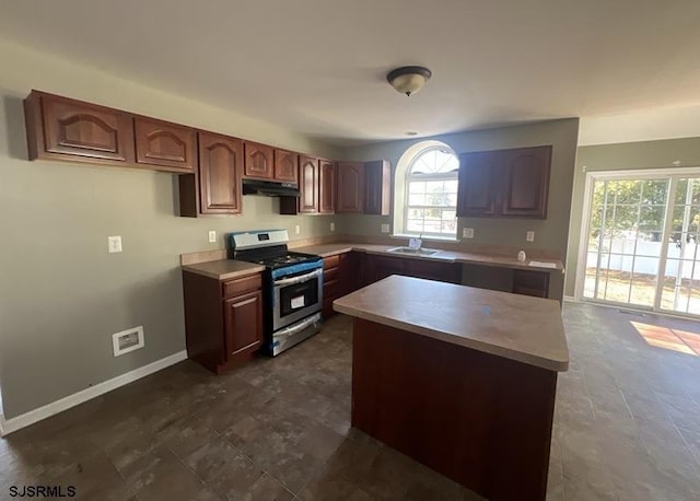 kitchen featuring light countertops, gas stove, a sink, under cabinet range hood, and baseboards