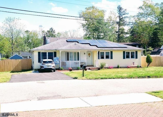 ranch-style home featuring a porch, a front yard, fence, and roof mounted solar panels