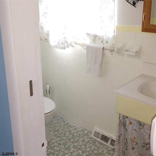 half bathroom with toilet, a healthy amount of sunlight, visible vents, and tile walls