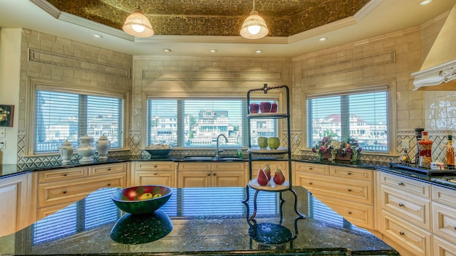 kitchen with decorative backsplash, a raised ceiling, dark stone countertops, crown molding, and a sink