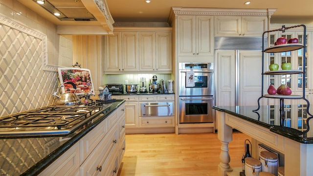 kitchen with a warming drawer, light wood finished floors, stainless steel appliances, decorative backsplash, and dark stone countertops