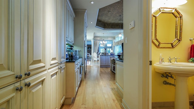 hallway with light wood-type flooring, a notable chandelier, and baseboards