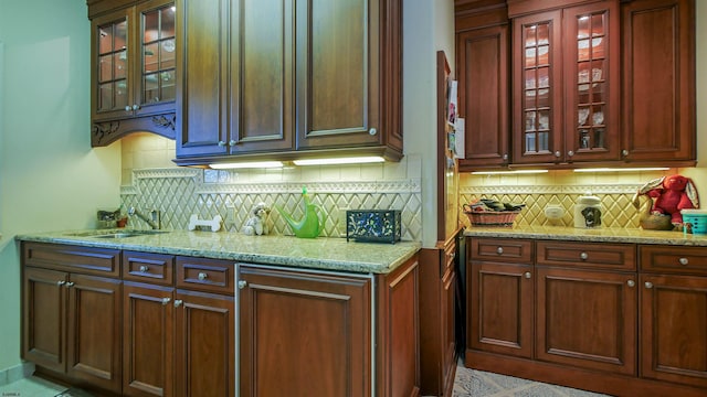 kitchen with light stone counters, glass insert cabinets, a sink, and decorative backsplash