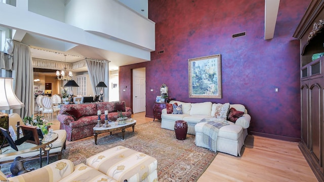 living room with an accent wall, wood finished floors, a high ceiling, and an inviting chandelier