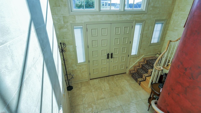 entryway featuring light tile patterned floors, stairs, and tile walls