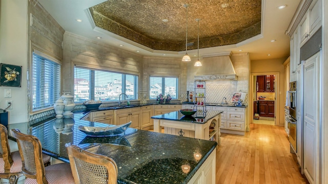 kitchen featuring a sink, premium range hood, a raised ceiling, and light wood-style floors