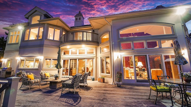 back of house at dusk featuring an outdoor hangout area, a chimney, a balcony, and stucco siding