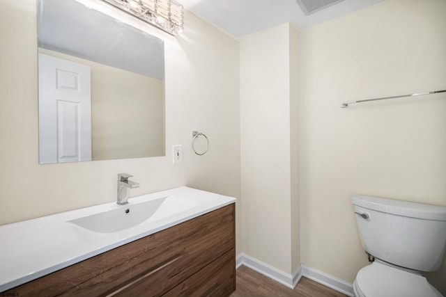 half bath featuring visible vents, toilet, vanity, wood finished floors, and baseboards